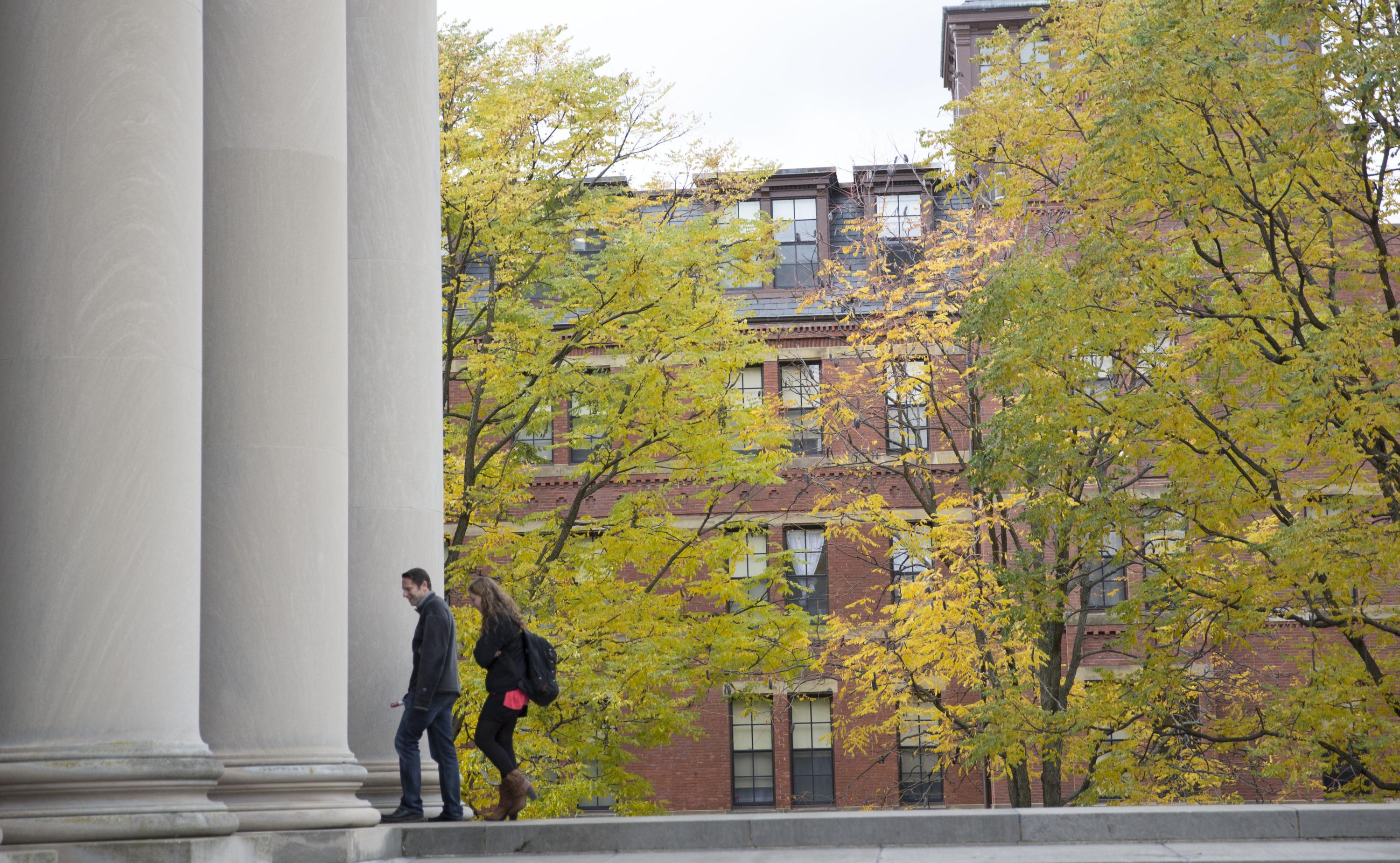 students walking into a building with large pillars. it appears to be a spring or fall day.