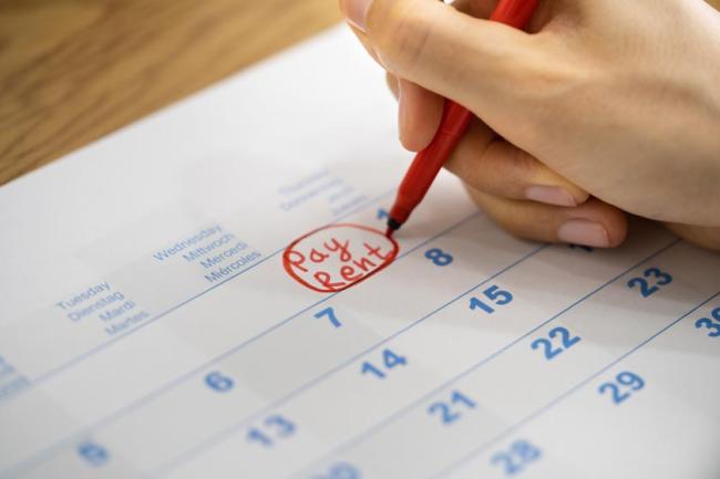 A hand writing "Pay Rent" with red pen on the first day of the month in a calendar. 