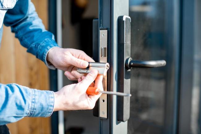 A close-up view of a man's hands changing core of a door lock in a glass door.