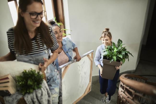 three roommates moving in together, walking up stairs and carrying belongings