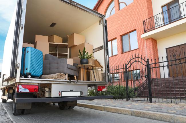 the back of a moving truck, open, full of cardboard boxes and parked in front of a residential building.