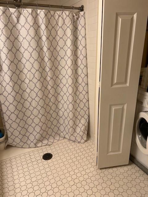 Bathroom with stacked washer and dryer in a closet, tiled floors, and a shower with a shower curtain.