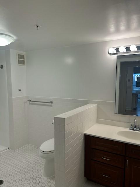 Primary bathroom with vanity, toilet, sinke, shower, and white tiling