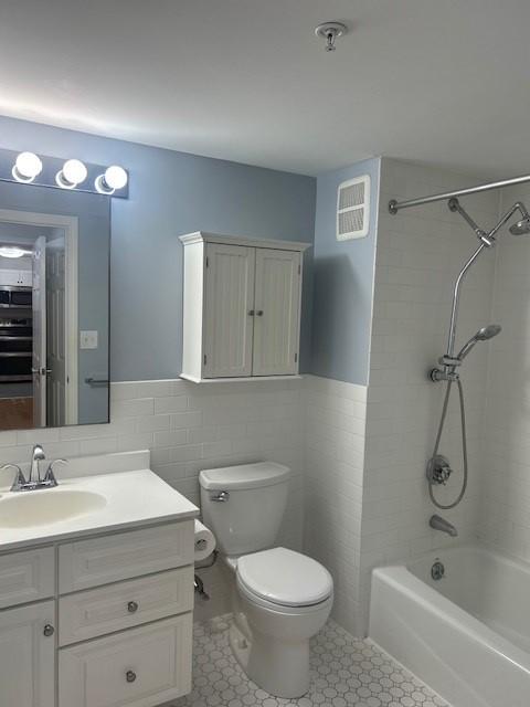 Primary bathroom with tub + shower, white tile flooring, toilet, and a vanity with sink and lower cabinetry