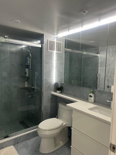 primary bathroom with glass shower door, stand-up shower, toilet, mirror, and vanity
