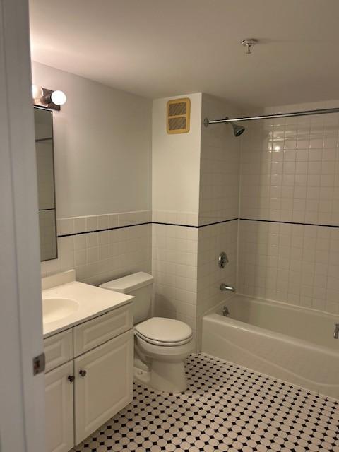 secondary bathroom with white tiling, walls, shower/tub combo, toilet, and vanity
