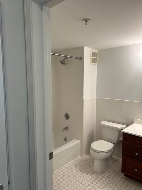 primary bathroom with white tiling, walls, shower/tub combo, toilet, and vanity