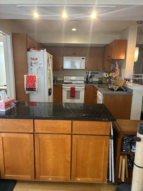 Kitchen with white appliances, dark counters, and wood cabinetry