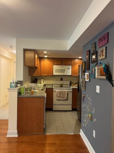 Kitchen with white appliances, wood cabinetry, tile flooring, and grey countertops. 
