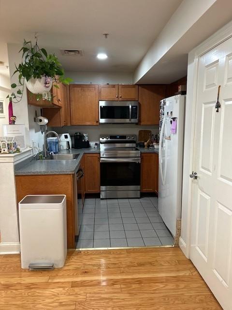 Kitchen with stainless steel appliances and a white fridge, tile flooring, wood cabinetry, and grey countertops